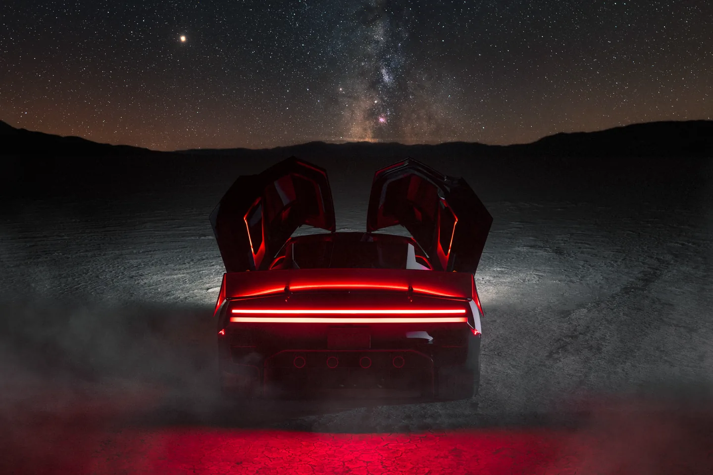 Rear of the Tesla Roadster at night, both doors raised, with the red light bar and rear wing lit